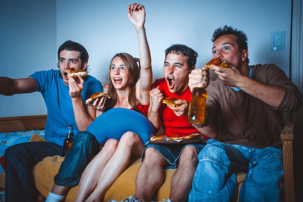 football fans on the couch near the TV with pizza and beer during the broadcast of the match