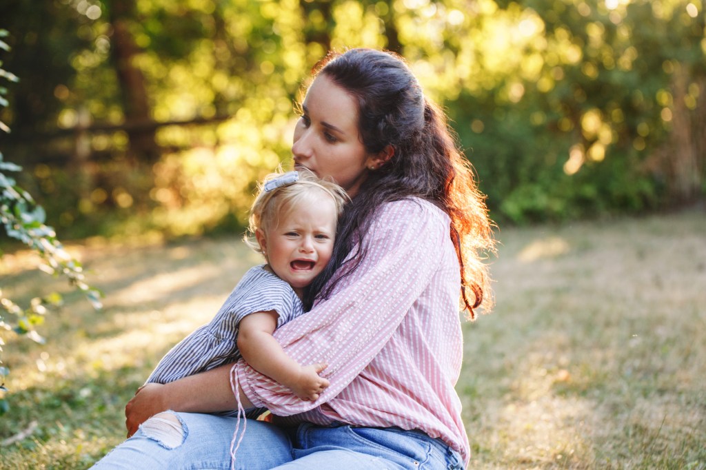 A young mother comforting her upset and crying toddler daughter in an outdoor park