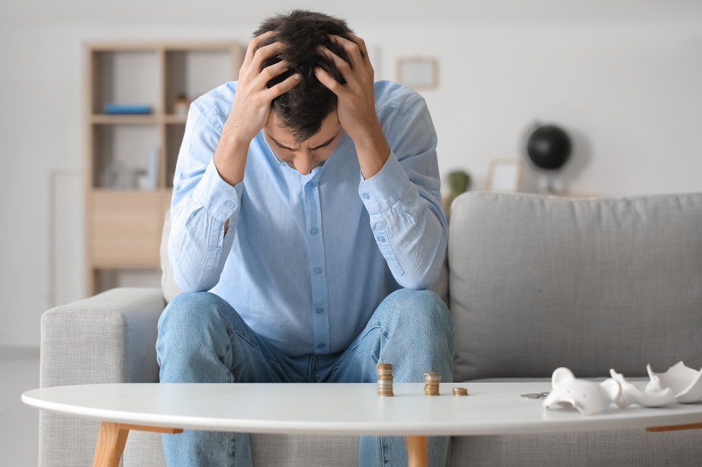 Distressed man sitting on a couch at home with coins, depicting a concept of bankruptcy