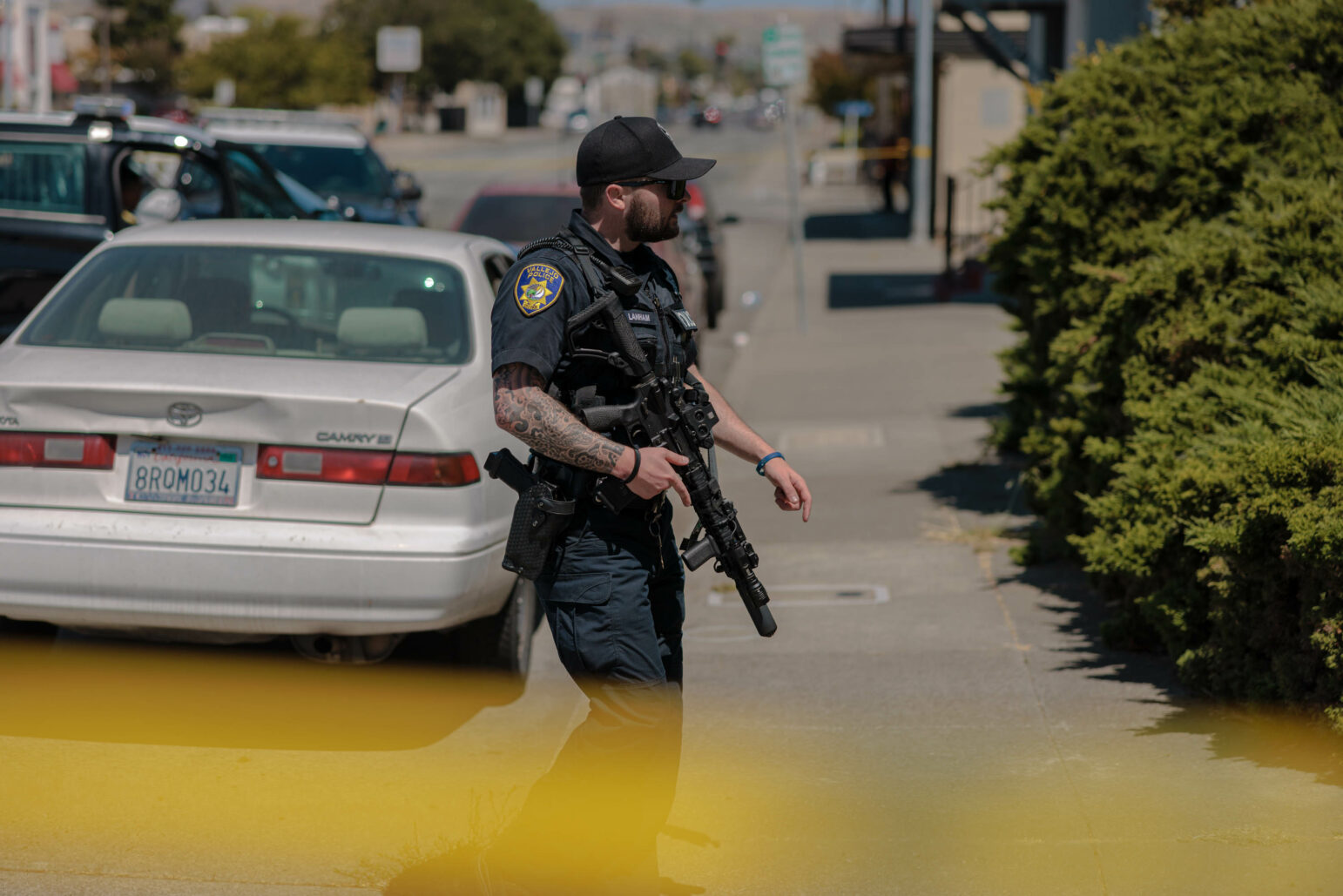 A police officer holding a rifle approaches a residence during daytime.