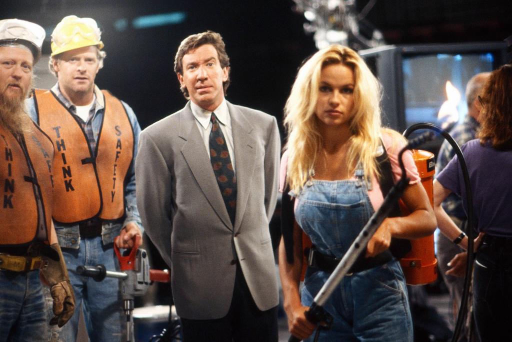 Pamela Anderson holding a pitchfork on the "Home Improvement" set with Mickey Jones and Tim Allen.