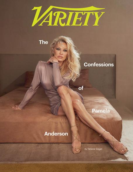 Pamela Anderson posing on a bed in a brown dress.