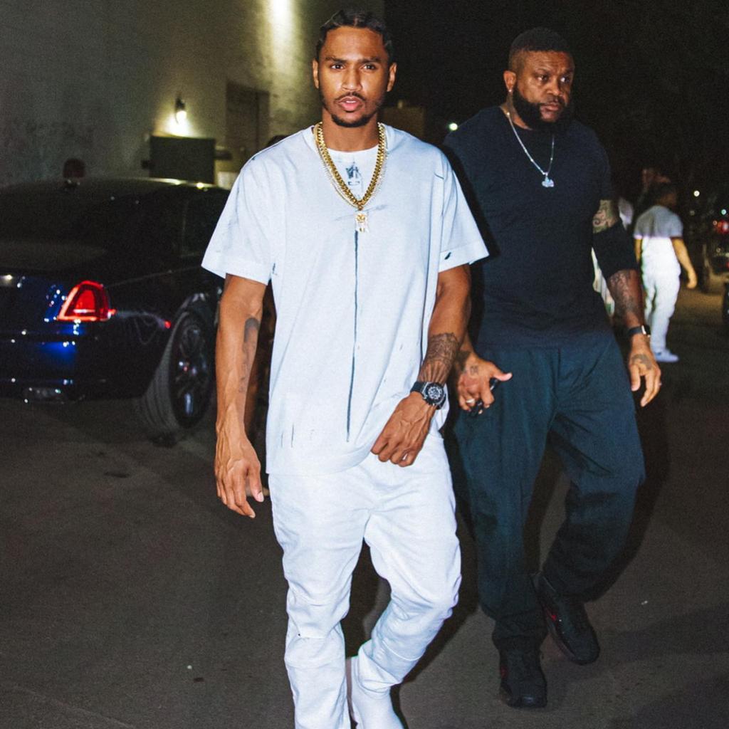 Trey Songz walking outside with a bodyguard beside him.