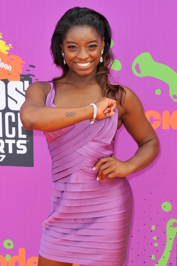 Simone Biles holds her forearm up to reveal her Olympic rings tattoo