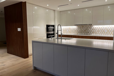 Example of a large minimalist light wood floor and white floor kitchen design in Other with a single-bowl sink, recessed-panel cabinets, white cabinets, marble countertops, white backsplash, mosaic tile backsplash, black appliances, an island and white countertops