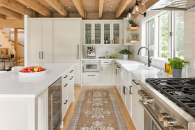 Transitional l-shaped light wood floor and exposed beam kitchen photo in Boston with a farmhouse sink, shaker cabinets, gray cabinets, quartz countertops, white backsplash, ceramic backsplash, paneled appliances, an island and white countertops