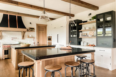 Example of a huge arts and crafts u-shaped medium tone wood floor, brown floor and exposed beam kitchen design in San Francisco with a farmhouse sink, recessed-panel cabinets, medium tone wood cabinets, quartz countertops, white backsplash, quartz backsplash, paneled appliances, two islands and white countertops