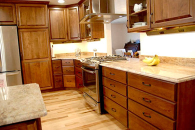Mid-sized elegant l-shaped light wood floor enclosed kitchen photo in Chicago with a double-bowl sink, raised-panel cabinets, medium tone wood cabinets, granite countertops, stainless steel appliances and an island