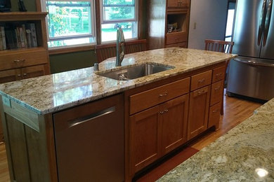 Example of a mid-sized classic single-wall light wood floor eat-in kitchen design in Minneapolis with an undermount sink, shaker cabinets, medium tone wood cabinets, granite countertops, brown backsplash, stainless steel appliances and an island