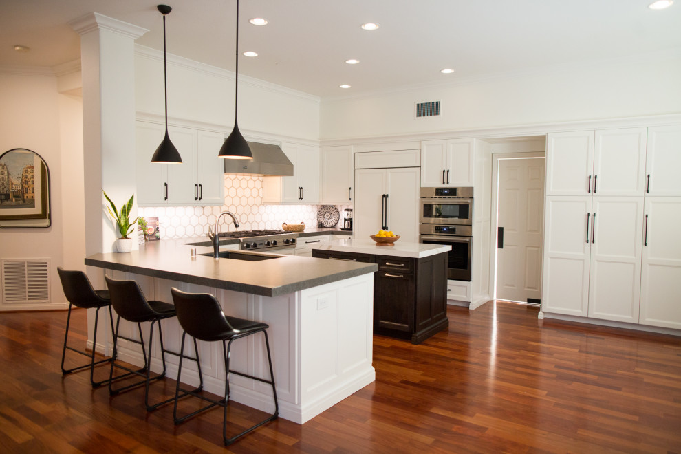 Example of a large classic u-shaped medium tone wood floor and brown floor eat-in kitchen design in San Diego with an undermount sink, white cabinets, white backsplash, porcelain backsplash, paneled appliances, two islands, gray countertops, recessed-panel cabinets and granite countertops