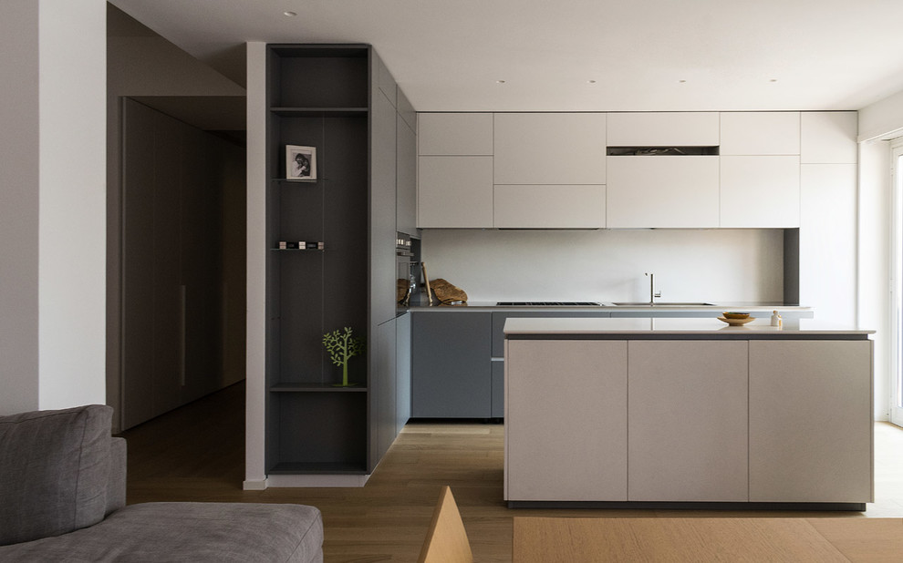 Mid-sized minimalist l-shaped light wood floor eat-in kitchen photo in Rome with an integrated sink, flat-panel cabinets, gray cabinets, stainless steel countertops, white backsplash, stainless steel appliances and an island