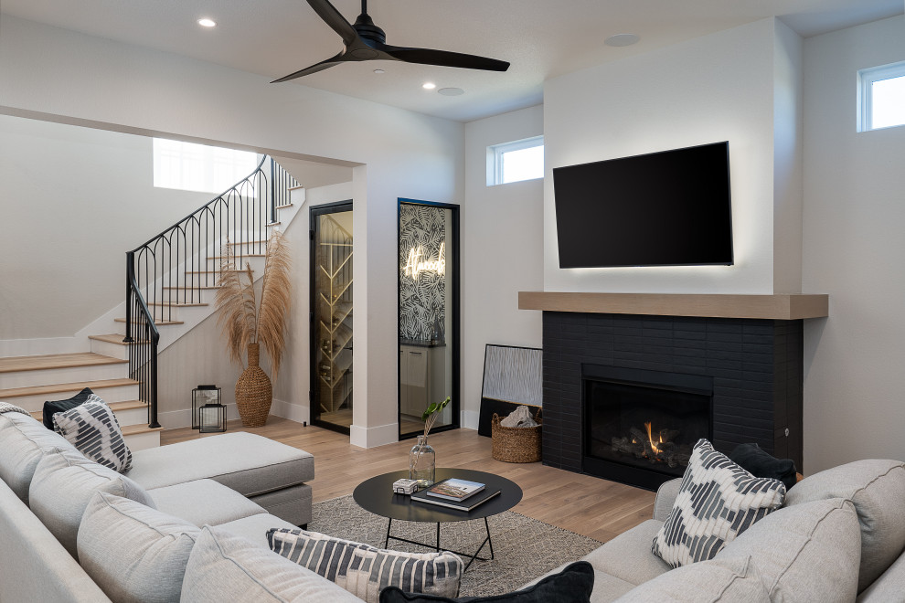 Design ideas for a large scandinavian open plan games room in Dallas with beige walls, light hardwood flooring, a standard fireplace, a brick fireplace surround, a wall mounted tv, beige floors and a chimney breast.
