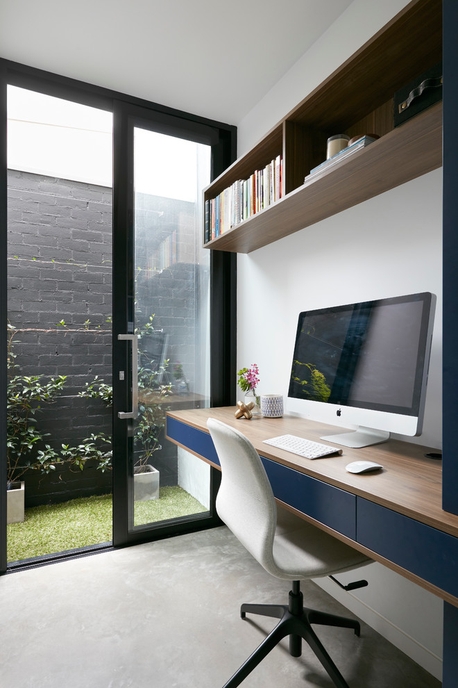 Trendy built-in desk concrete floor study room photo in Melbourne with white walls
