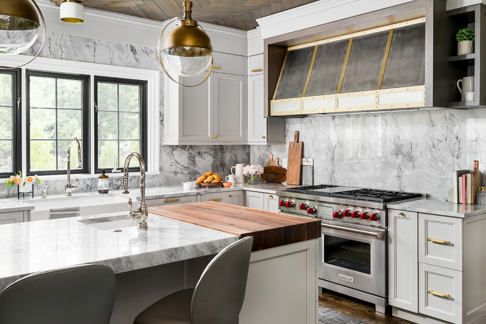 Mid-sized transitional l-shaped medium tone wood floor and brown floor enclosed kitchen photo in Chicago with a farmhouse sink, recessed-panel cabinets, gray cabinets, quartzite countertops, gray backsplash, stone slab backsplash, an island, gray countertops and stainless steel appliances