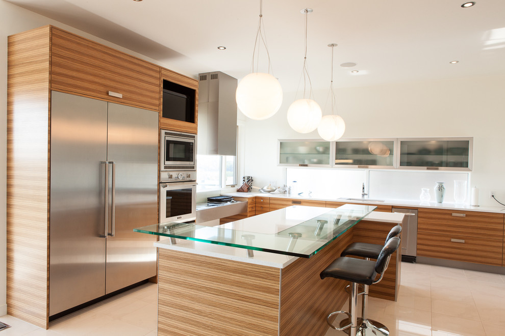Example of a minimalist l-shaped kitchen design in Edmonton with stainless steel appliances, glass countertops, an undermount sink, flat-panel cabinets and medium tone wood cabinets