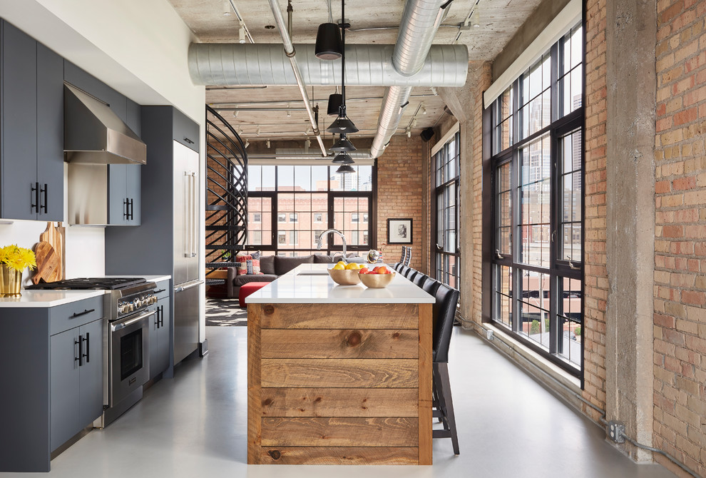 Inspiration for an industrial galley gray floor open concept kitchen remodel in Minneapolis with gray cabinets, stainless steel appliances, white countertops, an undermount sink, flat-panel cabinets, white backsplash and an island