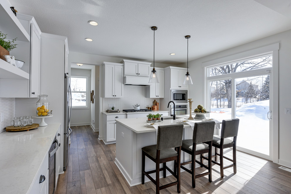 Inspiration for a small country l-shaped laminate floor and brown floor kitchen remodel in Minneapolis with an undermount sink, shaker cabinets, white cabinets, quartzite countertops, white backsplash, ceramic backsplash, stainless steel appliances, an island and white countertops