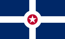 A blue flag with intersecting white lines and a red circle in the center that has a white star inscribed in it