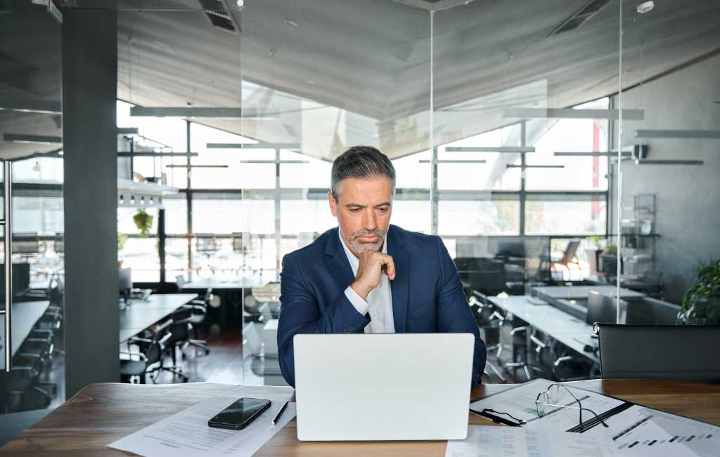 Busy serious mature business man ceo executive investor wearing suit looking at laptop computer analyzing financial risks, thinking over bank strategy working in office feeling doubt or concern.