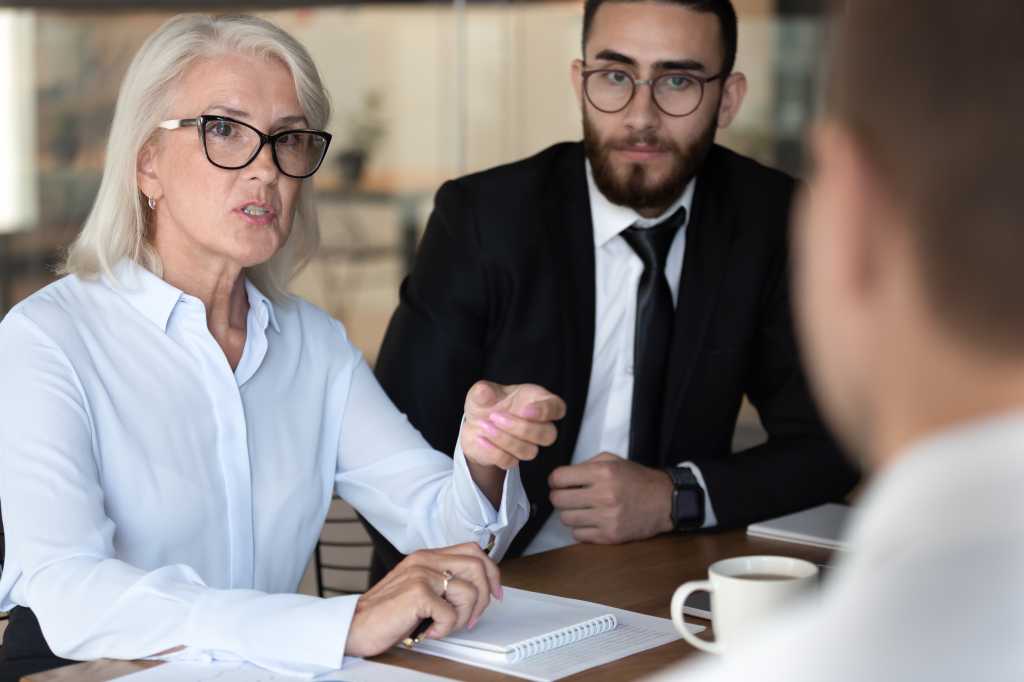 Negotiations lead by middle-aged boss talking with client diverse business people gathered together at boardroom, job interview process european and arabian HR managers interweaving applicant concept