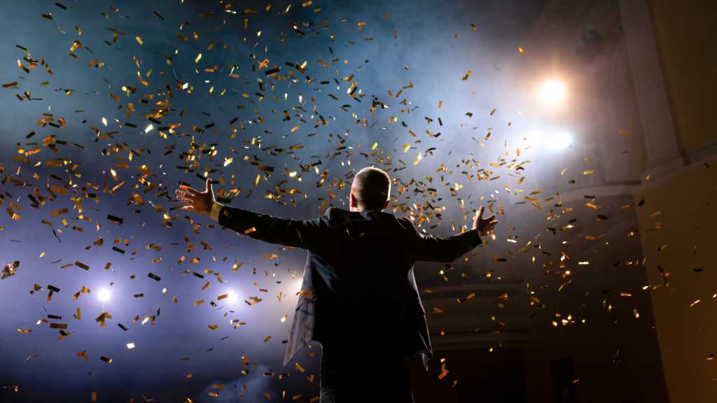 Successful businessman with arms up celebrating his victory. Celebrating success. Low angle view of excited young businessman keeping arms raised and expressing positivity while stands on the stage