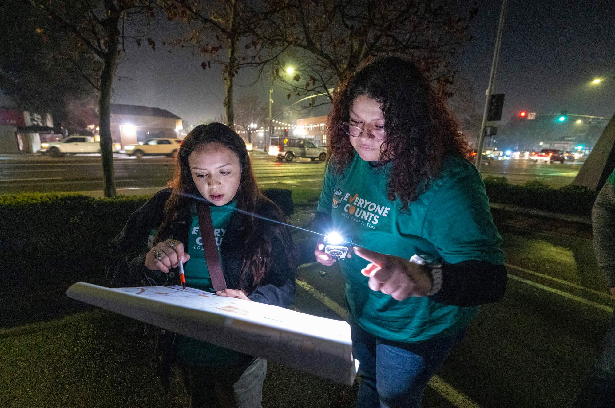 After speaking with a nearby homeless individual, volunteers Katherine Ibarra, left, of the Garden Grove Regional Center and Yolie Negrete, right, a program supervisor at City Net, check their map on where to go next as they stand in a parking lot on First Street in downtown Santa Ana before dawn on Tuesday morning, Jan. 23, 2024. This week hundreds of volunteers with the Everyone Counts, Point In Time, homeless survey, will gather data throughout Orange County that will help address homeless issues. (Photo by Mark Rightmire, Orange County Register/SCNG)