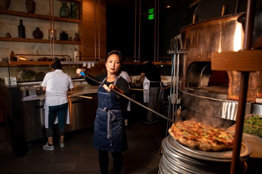 Ann Kim uses a long peel to add a pizza to an oven