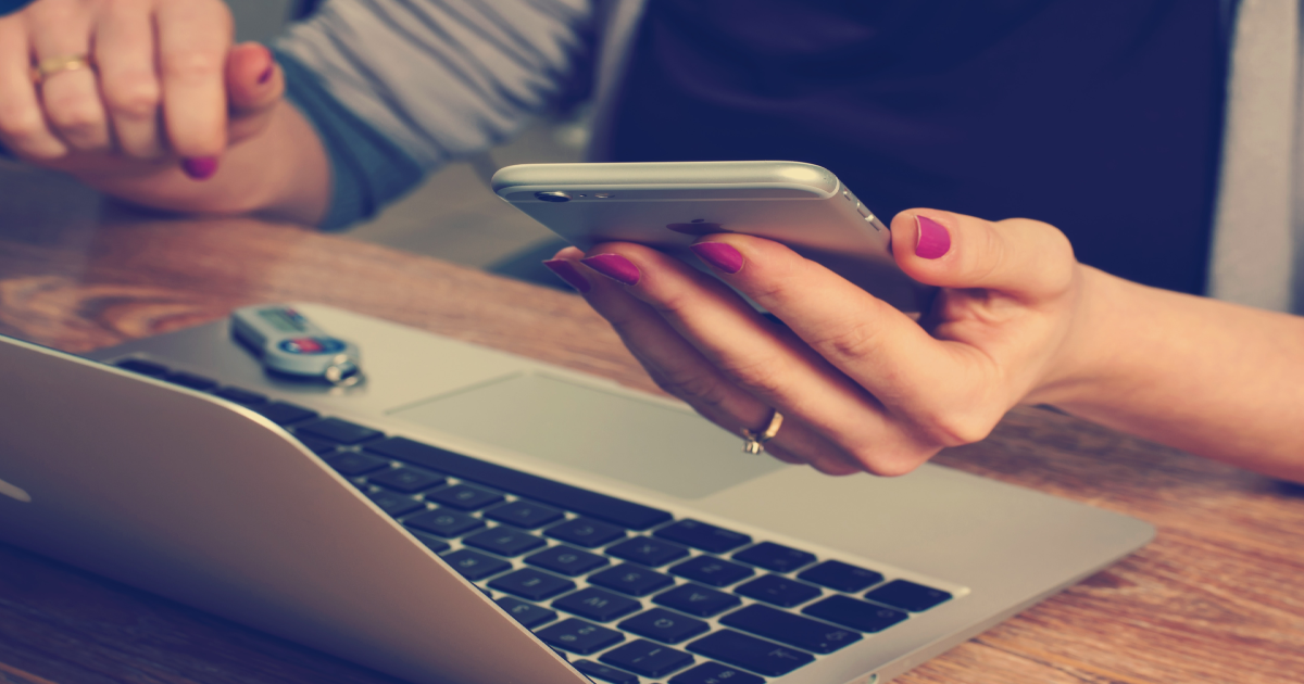 An image of a person checking their laptop for emails and their phone for text massages.