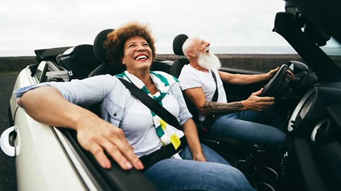 Una pareja conduce feliz un auto descapotado.