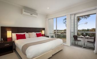 a large bed with white linens and red pillows is in a bedroom with a sliding glass door leading to an outdoor patio at Quest Sanctuary Lakes