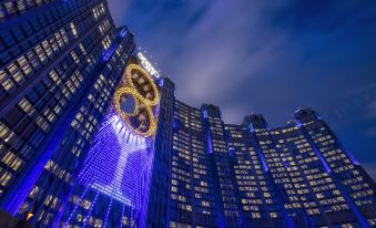 The world's largest hotel is illuminated at night against a backdrop of a blue sky and other surroundings at Studio City Hotel