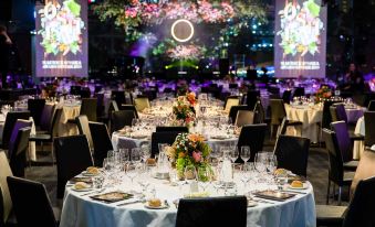 a well - decorated banquet hall with multiple tables set for a formal event , each table having its own unique arrangement of flowers and wine glasses at Oval Hotel at Adelaide Oval, an EVT hotel