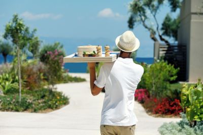 a man in a white shirt and hat is holding a tray with food on it at Ikos Dassia Ikos Dassia - All Inclusive Photo