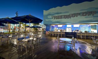 "a restaurant with tables and chairs , an umbrella , and a sign that says "" the shop ""." at Disney's Art of Animation Resort