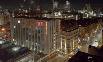 a city street at night , with buildings lit up and cranes visible in the background at voco MANCHESTER - CITY CENTRE