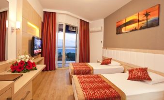 a hotel room with two beds , a tv , and a balcony overlooking the ocean , decorated with red curtains at Gardenia Hotel