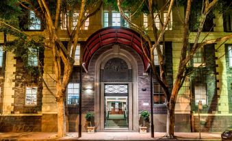 a city street at night , with a large tree - lined building in the background and an entrance to a building illuminated by lights at Oaks Sydney Goldsbrough Suites