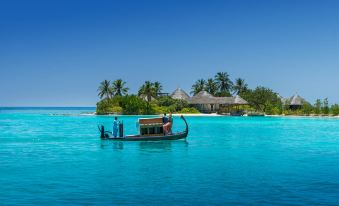 a group of people are rowing a boat in a blue ocean , with a small island in the background at Four Seasons Resort Maldives at Kuda Huraa