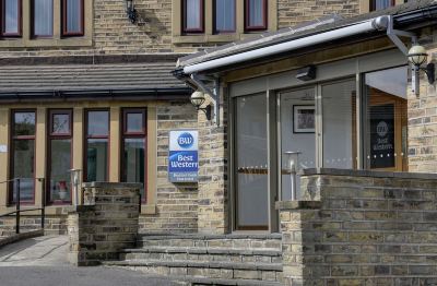 a brick building with a blue sign on the front door , surrounded by trees and other buildings at Best Western Bradford Guide Post Hotel Best Western Bradford Guide Post Hotel Photo