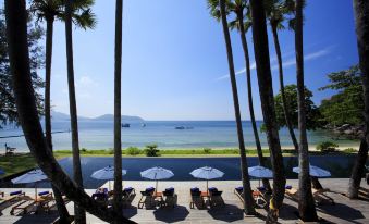 a sunny day at the beach , with several lounge chairs and umbrellas set up for people to relax and enjoy the view of the ocean at The Naka Phuket, a member of Design Hotels