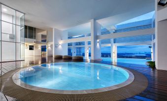 an indoor swimming pool surrounded by a building , with a view of the ocean in the background at Fraser Place Puteri Harbour, Johor