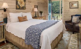 a cozy bedroom with a large bed , white linens , and a blue comforter , surrounded by wooden walls at Glen-Ella Springs Inn