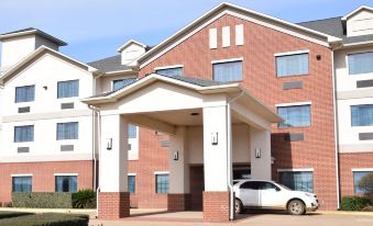 a brick hotel with a car parked in front and a white building with columns at Franklin Inn and Suites