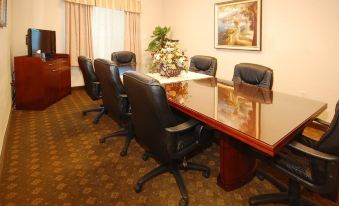 a conference room with a large wooden table surrounded by black chairs , and a vase of flowers on the table at Franklin Inn and Suites