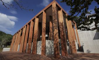 a modern wooden building with multiple levels and a central entrance , situated in a courtyard under a blue sky at The Naka Phuket, a member of Design Hotels