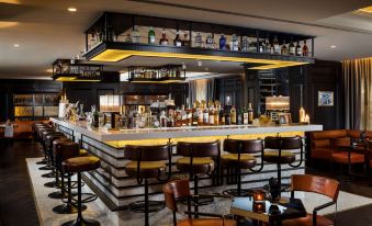 a modern bar with black and gold accents , featuring a bar area with multiple stools and shelves of liquor bottles at Hilton Vienna Plaza