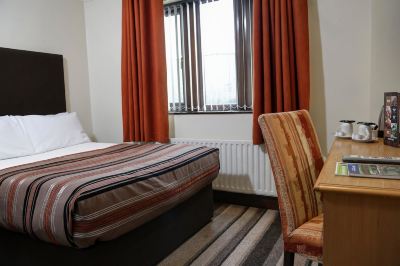 a hotel room with a bed , curtains , and a window , along with a striped chair and wooden nightstand at Best Western Bradford Guide Post Hotel Best Western Bradford Guide Post Hotel Photo