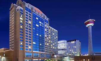 a large hotel building with a tower in the background , surrounded by other buildings and trees at Hyatt Regency Calgary