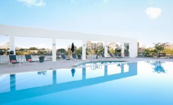 a large swimming pool with a white building in the background and lounge chairs around it at Stamford Plaza Brisbane