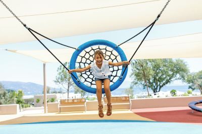 a young girl is swinging on a blue hammock in an outdoor setting , surrounded by trees at Ikos Dassia Ikos Dassia - All Inclusive Photo